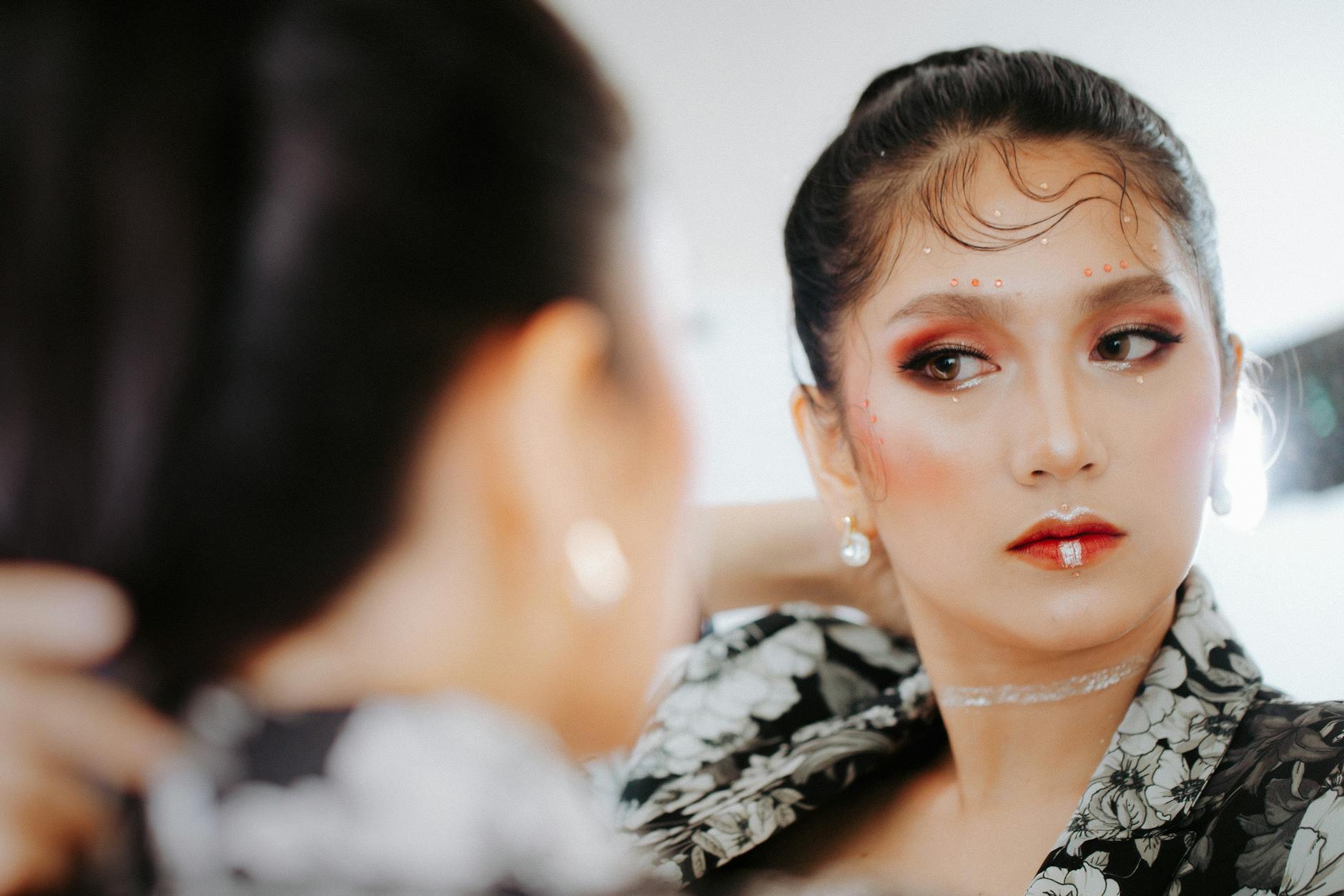 Efekt mokrej skóry w makijażu: jak uzyskać glow bez wrażenia tłustej cery przez cały dzień Elegancka kobieta nakłada makijaż przy lustrze, efekt glow na skórze